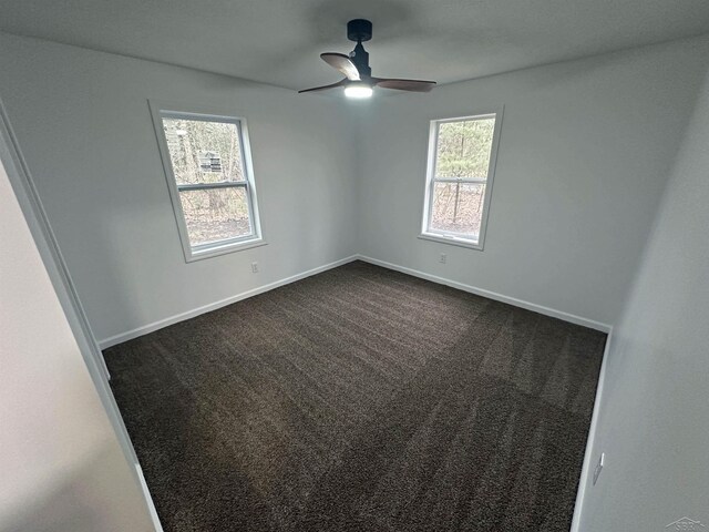 empty room with a ceiling fan, dark colored carpet, and baseboards