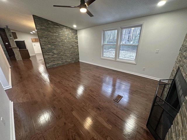 unfurnished living room featuring ceiling fan, lofted ceiling, a fireplace, baseboards, and dark wood-style floors