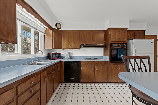 kitchen with black appliances, under cabinet range hood, a sink, light countertops, and light floors