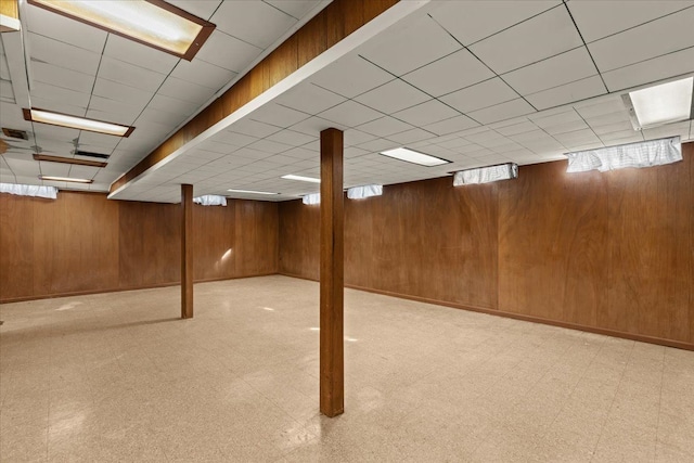 finished basement with tile patterned floors, a drop ceiling, baseboards, and wooden walls