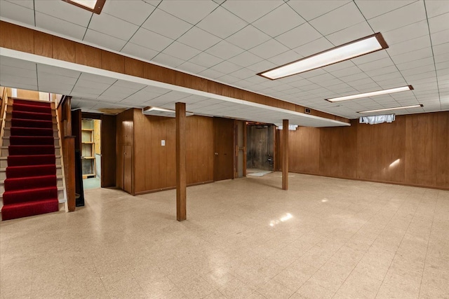 finished below grade area with tile patterned floors, stairway, wood walls, and a paneled ceiling