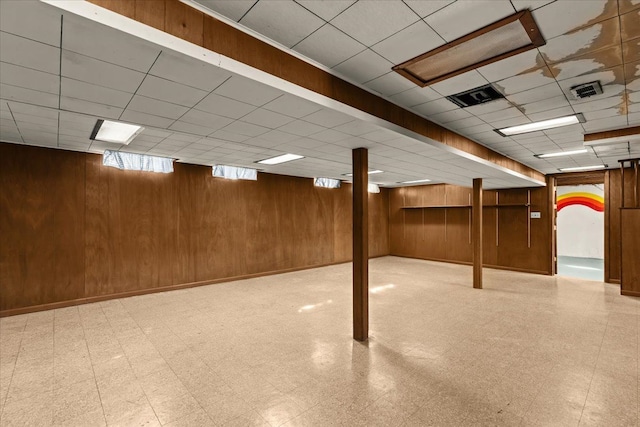 basement featuring tile patterned floors, wooden walls, and visible vents