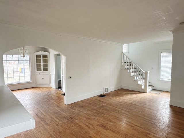 unfurnished living room with a wealth of natural light, arched walkways, stairway, and hardwood / wood-style flooring