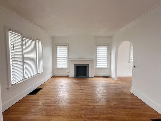 unfurnished living room with arched walkways, ornamental molding, wood finished floors, and visible vents