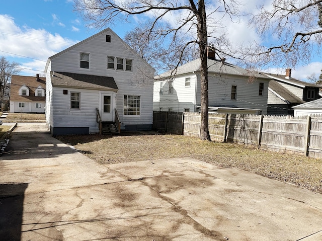 rear view of property with entry steps, a shingled roof, and fence