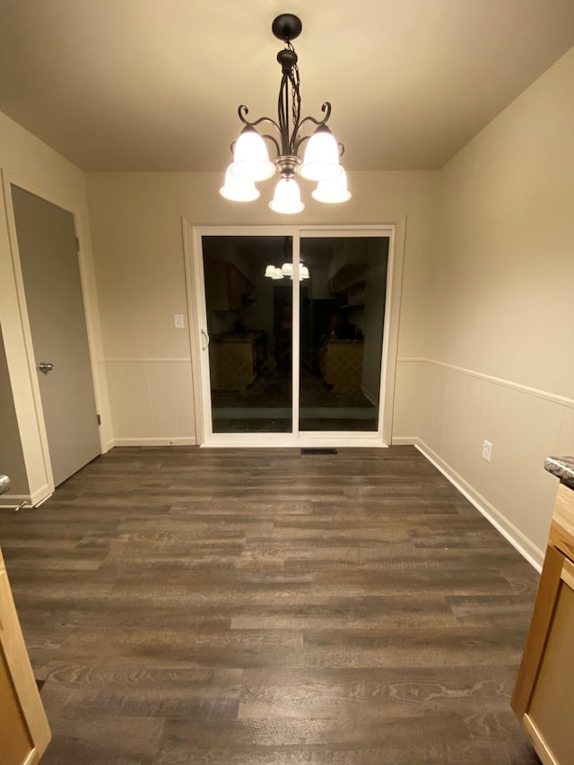 unfurnished dining area with dark wood-type flooring, wainscoting, and a notable chandelier