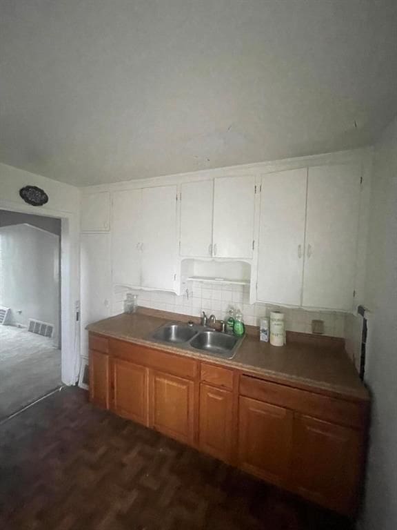 kitchen featuring arched walkways, visible vents, backsplash, brown cabinetry, and a sink