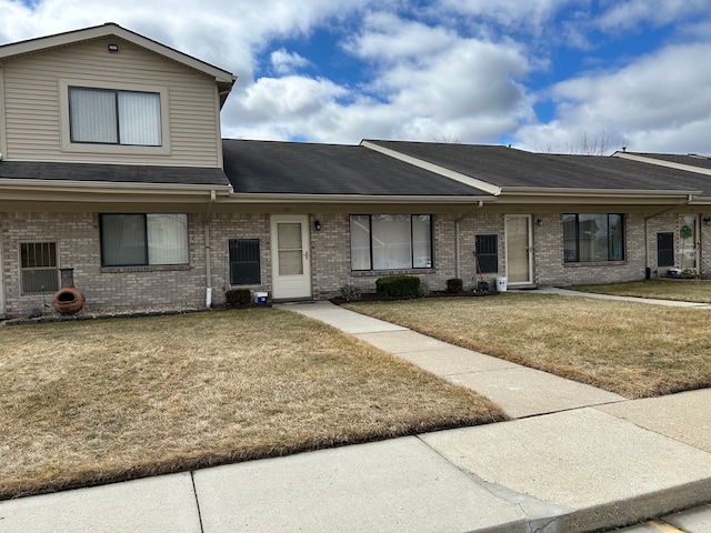 townhome / multi-family property with a front lawn, roof with shingles, and brick siding