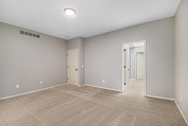 spare room with baseboards, visible vents, a textured ceiling, and light colored carpet