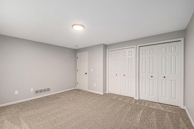 unfurnished bedroom featuring baseboards, carpet floors, visible vents, and multiple closets