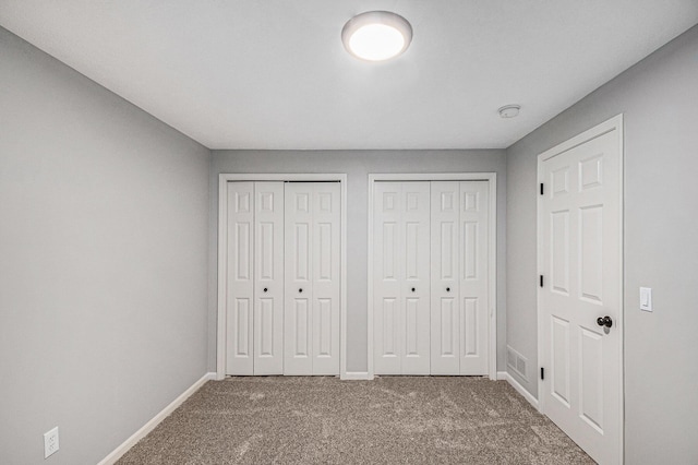 unfurnished bedroom featuring multiple closets, carpet flooring, visible vents, and baseboards