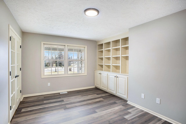 empty room with dark wood-style floors, built in shelves, baseboards, and a textured ceiling