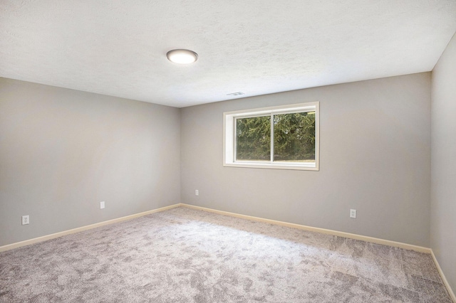 empty room with a textured ceiling, carpet flooring, visible vents, and baseboards