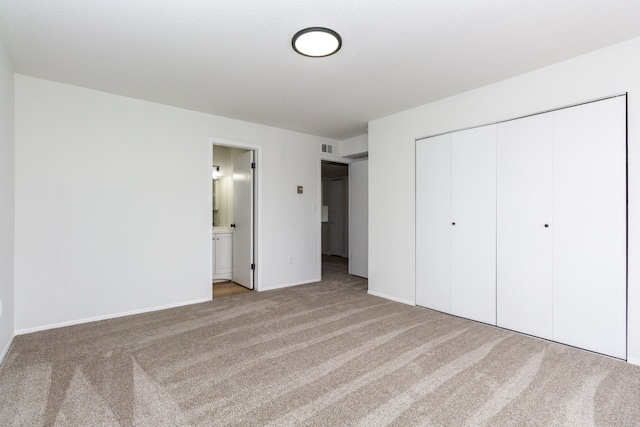 unfurnished bedroom featuring carpet floors, visible vents, baseboards, a closet, and ensuite bath