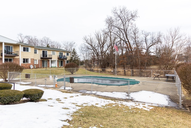 snow covered pool with a community pool, fence, and a yard