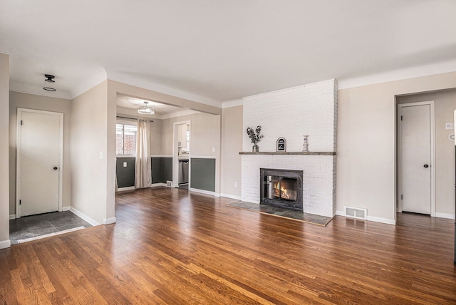 unfurnished living room with a brick fireplace, visible vents, baseboards, and wood finished floors