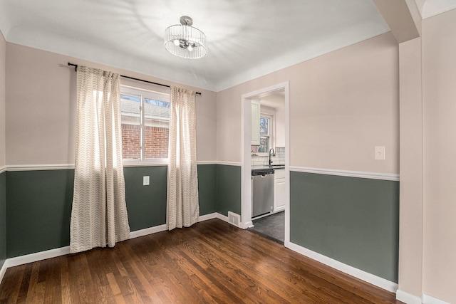 spare room with an inviting chandelier, a sink, dark wood finished floors, and baseboards