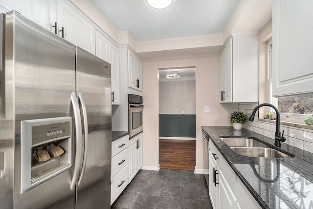 kitchen with a sink, white cabinetry, appliances with stainless steel finishes, backsplash, and dark stone countertops