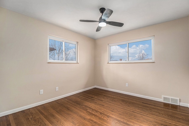 empty room with baseboards, dark wood-style flooring, visible vents, and a healthy amount of sunlight