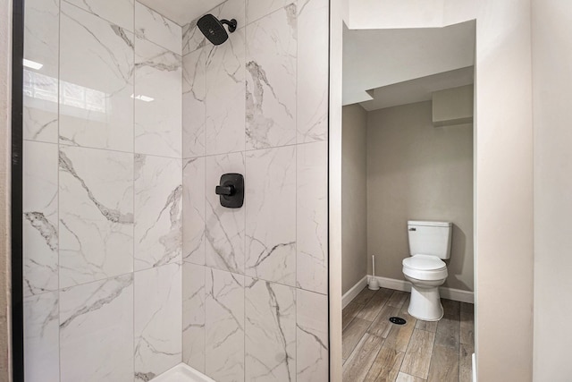 full bathroom featuring toilet, wood tiled floor, baseboards, and a tile shower