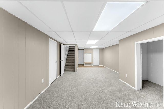 finished basement featuring a paneled ceiling, stairs, and carpet flooring