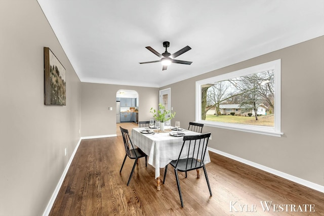 dining space featuring arched walkways, ceiling fan, baseboards, and wood finished floors