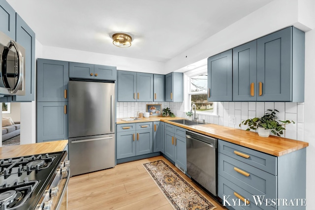 kitchen featuring tasteful backsplash, stainless steel appliances, light wood-type flooring, wooden counters, and a sink