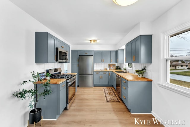 kitchen with butcher block counters, appliances with stainless steel finishes, backsplash, and a sink