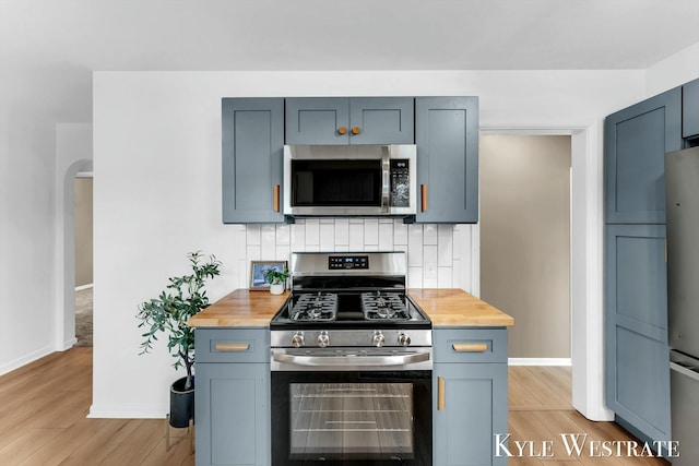 kitchen with light wood-style floors, tasteful backsplash, stainless steel appliances, and wooden counters