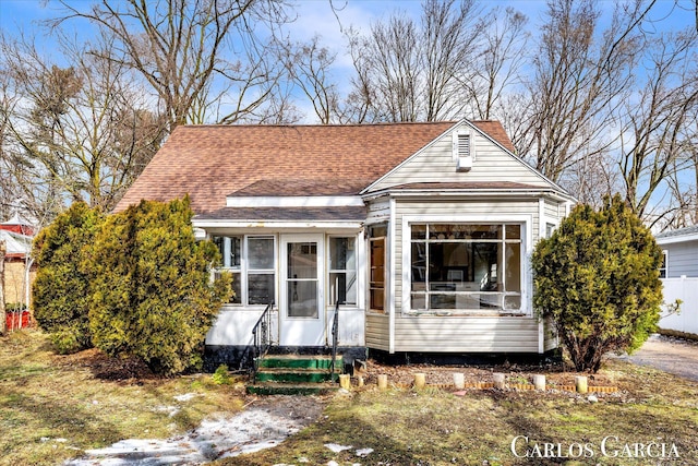 view of front facade with entry steps, roof with shingles, and a sunroom