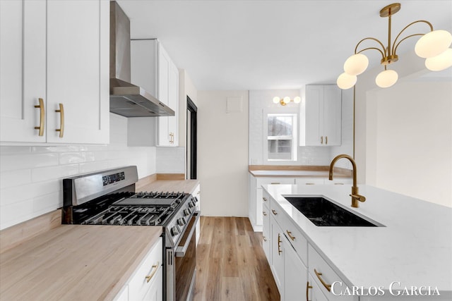 kitchen featuring light wood-style flooring, white cabinetry, a sink, gas range, and wall chimney exhaust hood