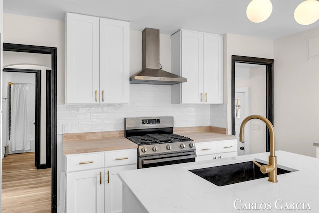 kitchen with backsplash, stainless steel range with gas stovetop, a sink, white cabinetry, and wall chimney exhaust hood