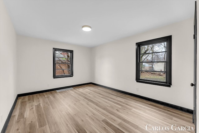 spare room with light wood-type flooring, visible vents, and baseboards