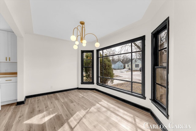 unfurnished dining area featuring baseboards, light wood-style flooring, and an inviting chandelier