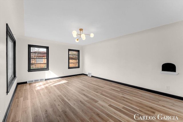 spare room featuring an inviting chandelier, baseboards, visible vents, and wood finished floors