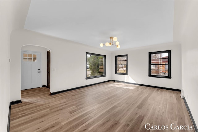 spare room with light wood-style flooring, visible vents, arched walkways, and baseboards