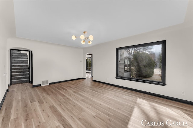 spare room featuring arched walkways, visible vents, stairway, an inviting chandelier, and wood finished floors