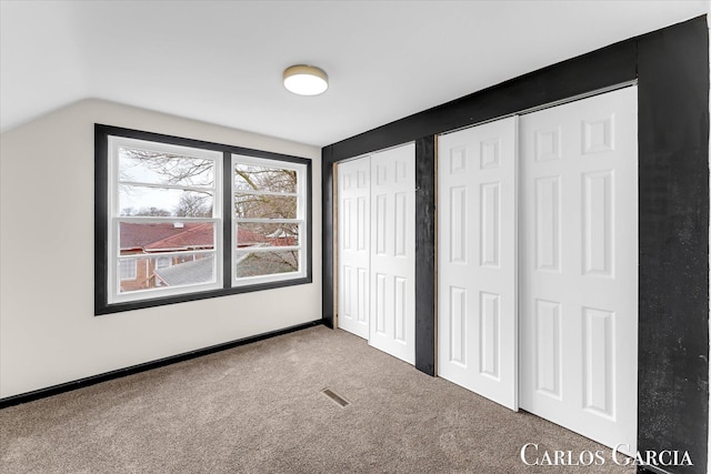 unfurnished bedroom with visible vents, baseboards, vaulted ceiling, carpet, and two closets