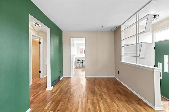 empty room featuring a wealth of natural light, wood finished floors, visible vents, and baseboards