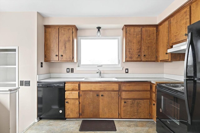 kitchen with light countertops, brown cabinetry, a sink, under cabinet range hood, and black appliances