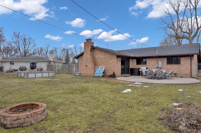 back of house with an outdoor fire pit, brick siding, fence, a lawn, and a chimney