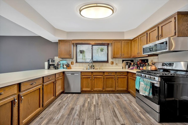 kitchen featuring light wood-style flooring, a sink, light countertops, appliances with stainless steel finishes, and brown cabinetry