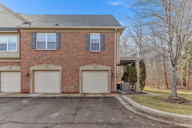 view of front of property with brick siding, central AC unit, an attached garage, and roof with shingles