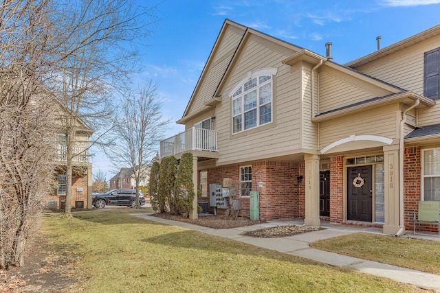 townhome / multi-family property with a front lawn, a balcony, and brick siding