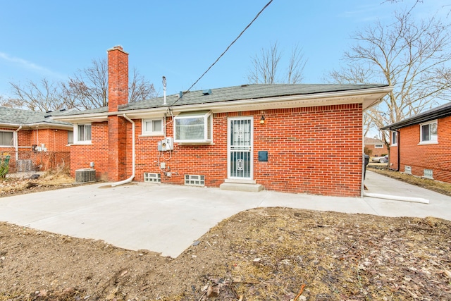 rear view of house with entry steps, central AC, brick siding, a chimney, and a patio area