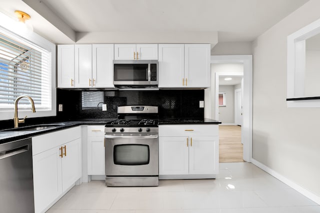 kitchen featuring a sink, white cabinetry, appliances with stainless steel finishes, decorative backsplash, and baseboards