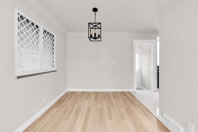 unfurnished dining area with a notable chandelier, wood finished floors, visible vents, and baseboards