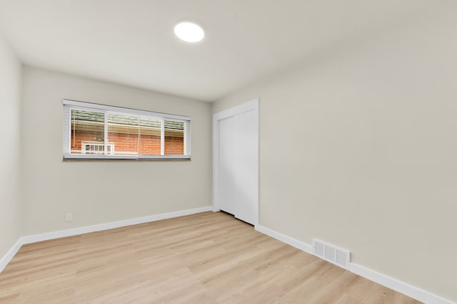 empty room with visible vents, light wood-type flooring, and baseboards