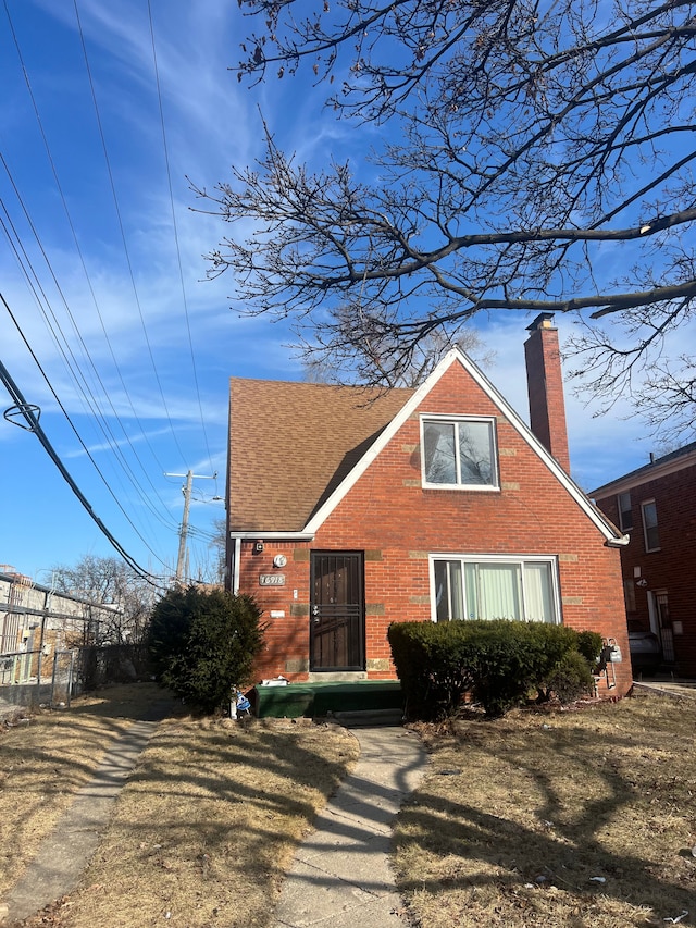 view of front facade featuring brick siding, a chimney, and a shingled roof