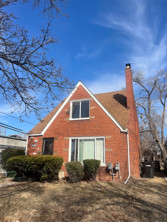 rear view of property with brick siding, roof with shingles, and a chimney